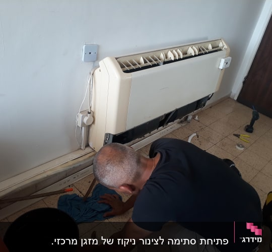 אדם מתקן מזגן קיר עם כלים על הרצפה